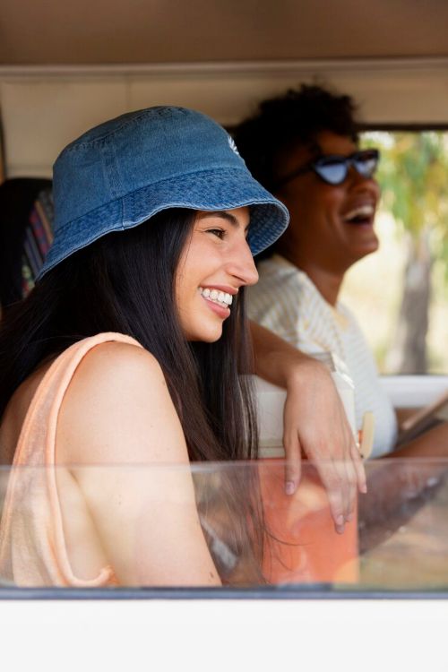 Hombre y mujer vestidos de traje sentados en la parte trasera de un automóvil, sonriendo mientras miran juntos la pantalla de un teléfono móvil